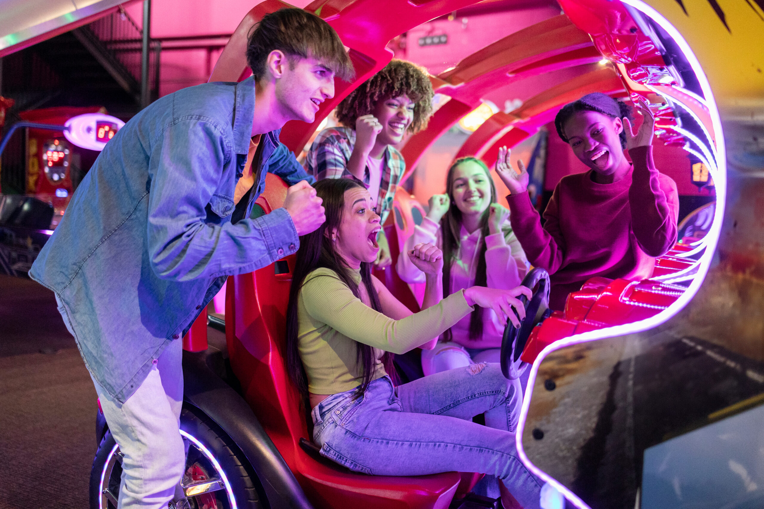 group of multiracial friends having fun playing video arcade and dancing in a night room with neon lights